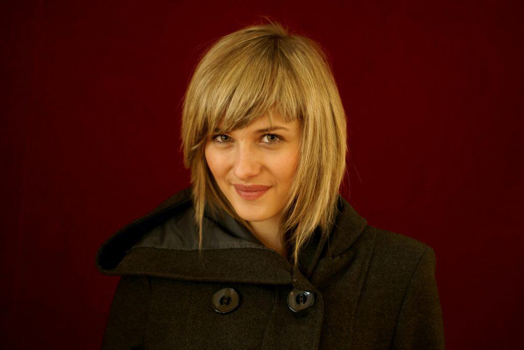 Chic fashion portrait of a woman in a dark coat with a striking red background.